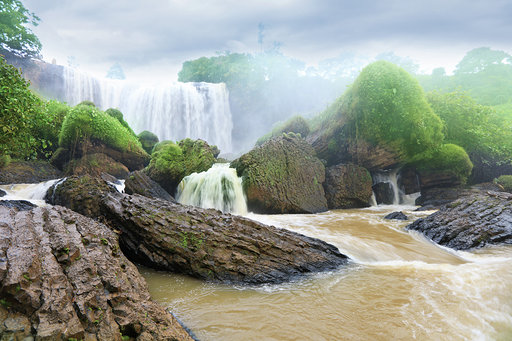 Amazing view of waterfall with yellow water among green woods on dramatic sky background in Dalat, Vietnam..