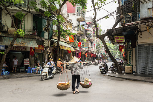 Hanoi, Vietnam - May 19, 2016: Street vendor carrying transporting goods in baskets using a carrying pole, also called a shoulder pole, in Hanoi's Old Quarter.