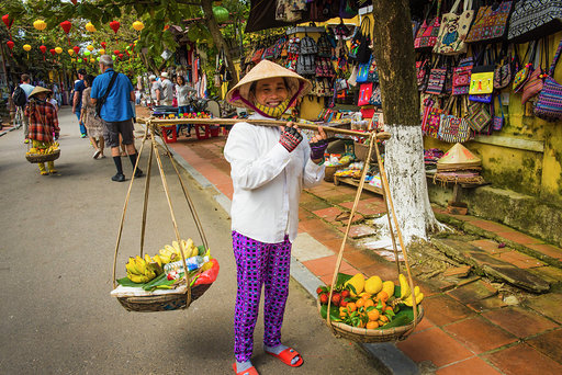 Hoi An, Vietnam. January 13, 2017: Vietnamese woman carrying baskets of fresh fruit that she sells along the streets of Hoi An. The sellers usually ask tourists if they want to take a picture, in exchange for money